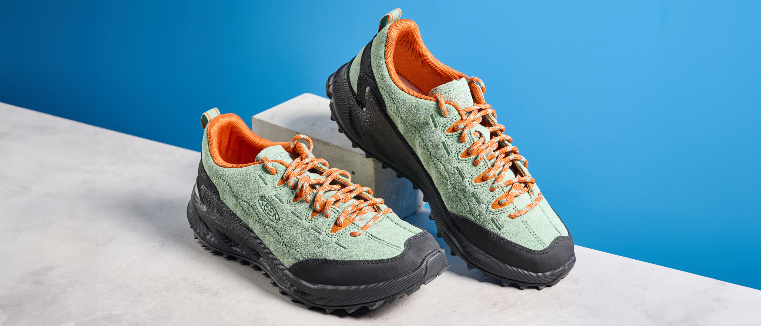 the keen jasper zionic hiking shoes in green/gold colorway photographed against a blue tom&#039;s guide background and a stone floor, showing the lug sole and the leather upper with orange laces