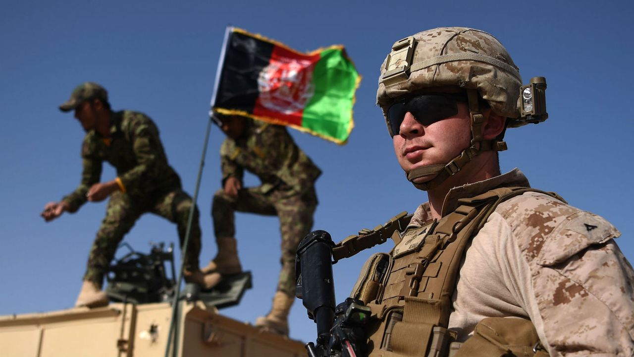 A US Marine looks on as Afghan National Army soldiers raise the Afghan National flag