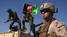 A US Marine looks on as Afghan National Army soldiers raise the Afghan National flag