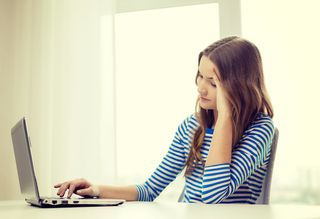 A teen girl sits at her computer, looking sad