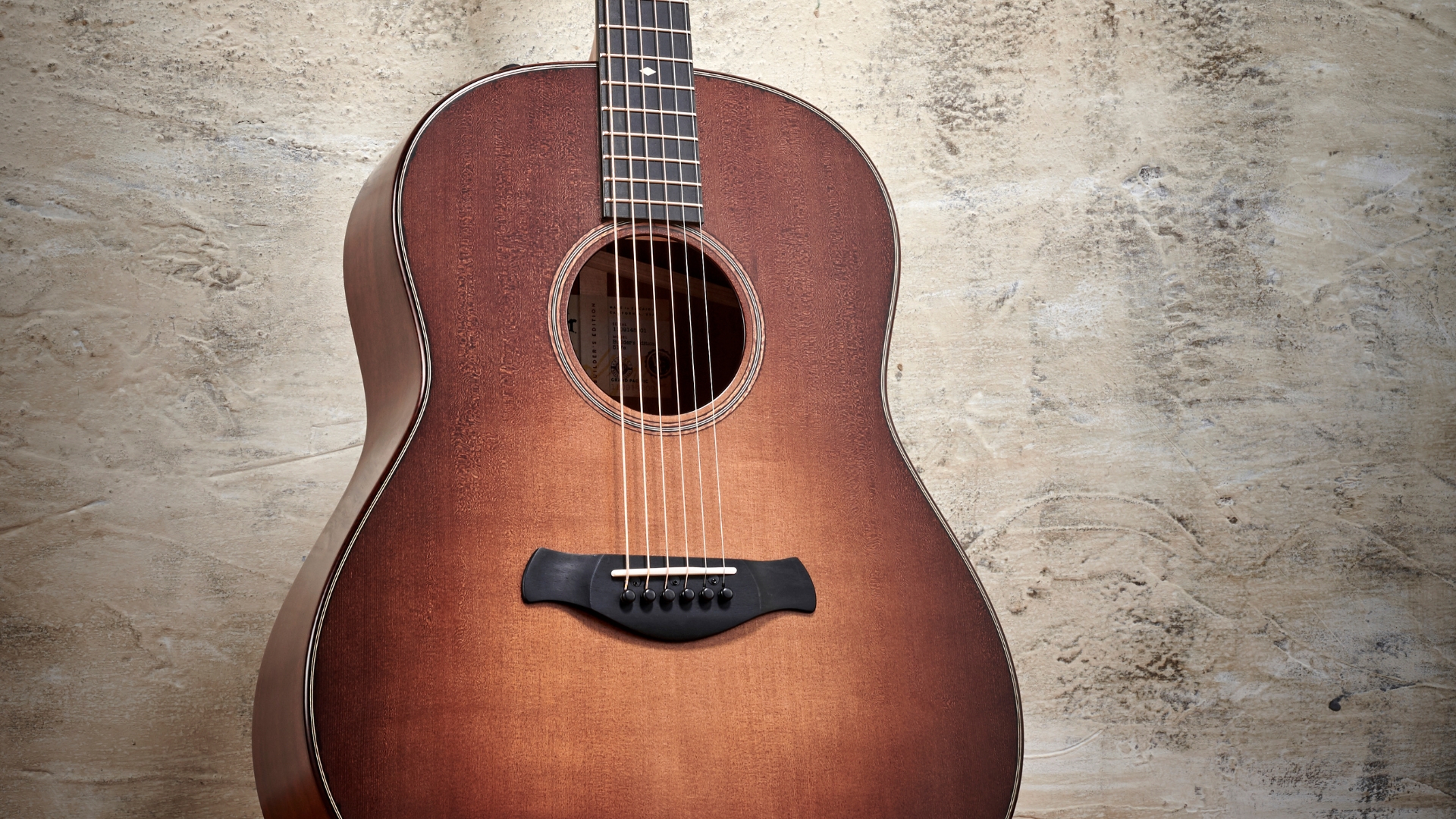 A Taylor Builder’s Edition 517e acoustic guitar leaning against a concrete wall