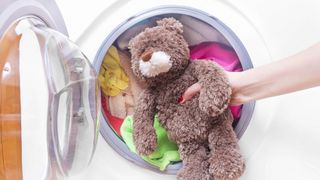 A teddy bear in front of a loaded washing machine