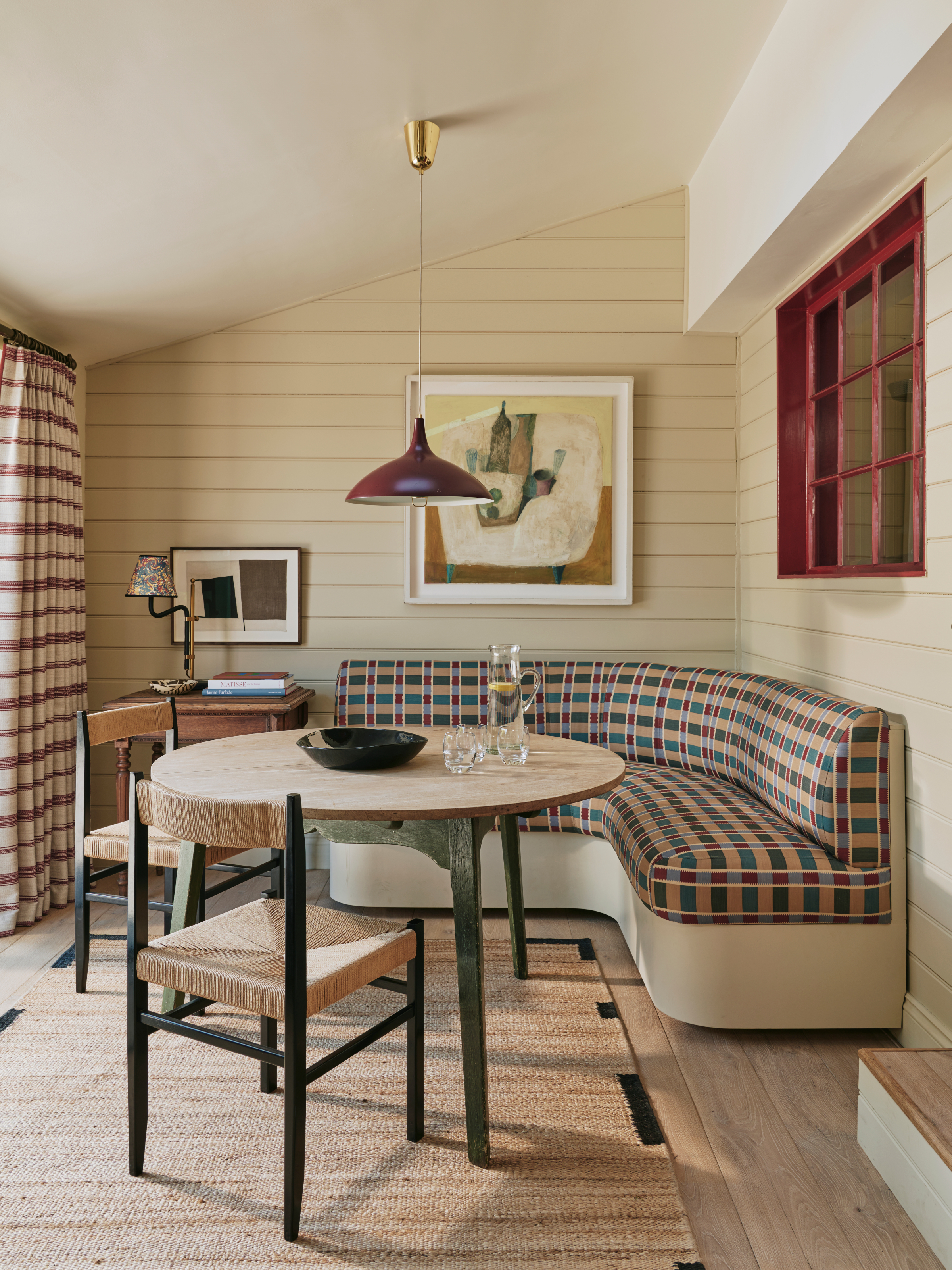 Cream panelled breakfast nook with curved banquette seating in check pattern, round dining table and woven chairs