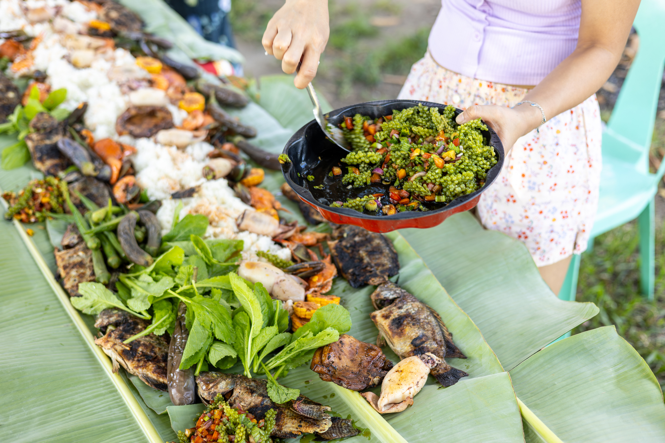 Young adult Filipino Southeast Asian woman serving arusip seaweed grape dish as part of a traditional Filipino Boodle fight incorporating a diverse range of Filipino foods, Tarlac Province, Central Luzon, Philippines, South East Asia