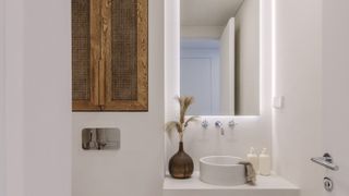 cream bathroom with microcement walls, vanity, white countertop sink, chrome wall mounted taps mirror above sink and wooden cupboard doors integrated into wall