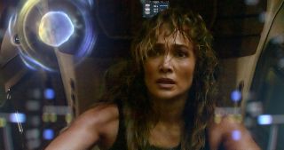 a woman (jennifer lopez) sits in a spaceship, as circular reflections shine off a glass pane in front of her