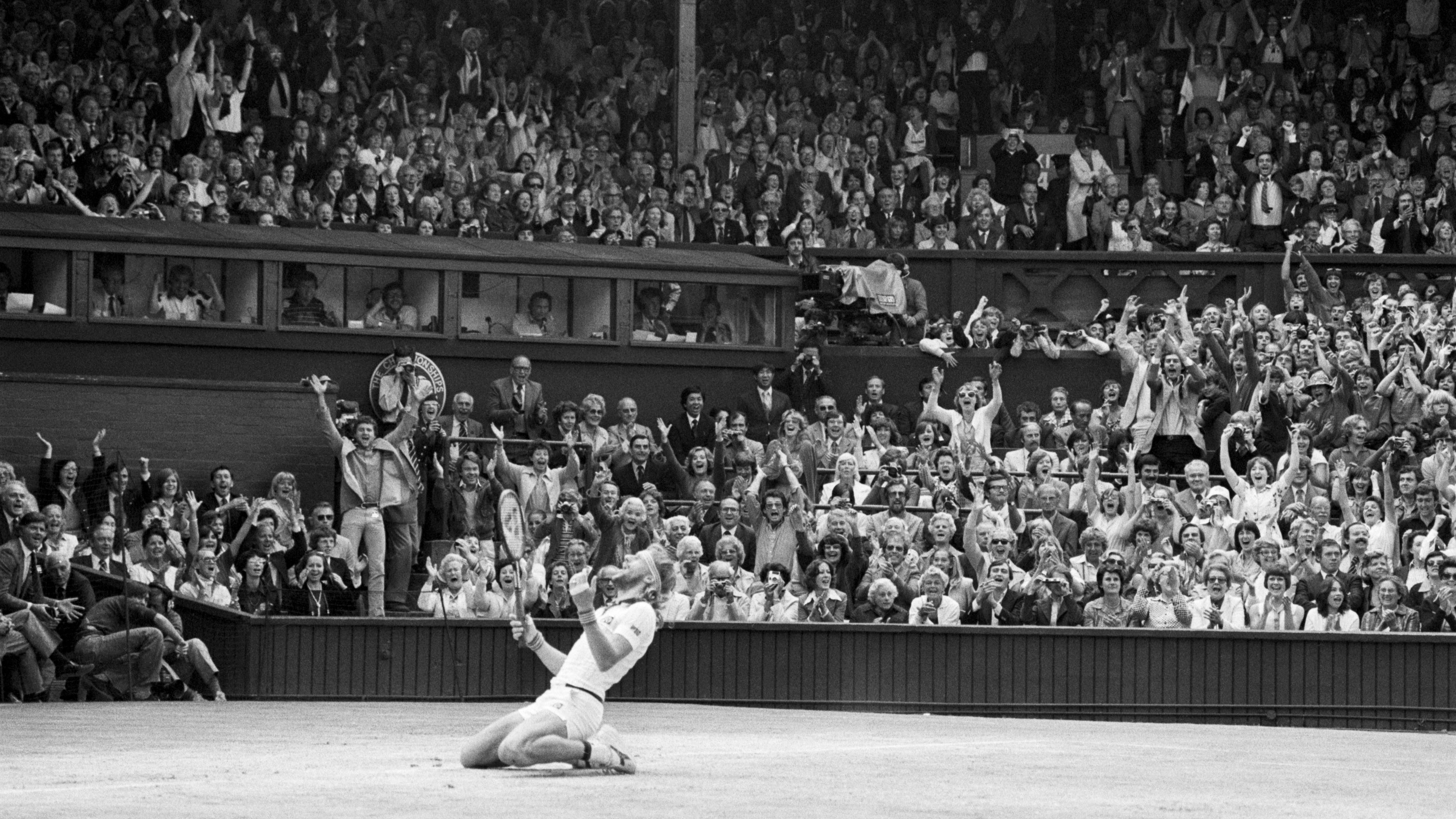 Bjorn Borg sinks to knees after making the winning shot in the final set at Wimbledon, to win the title for the 5th consecutive time. The crowd background yell their approval.