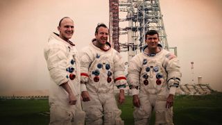 Three astronauts poses in front of their Saturn V rocket and Apollo spacecraft