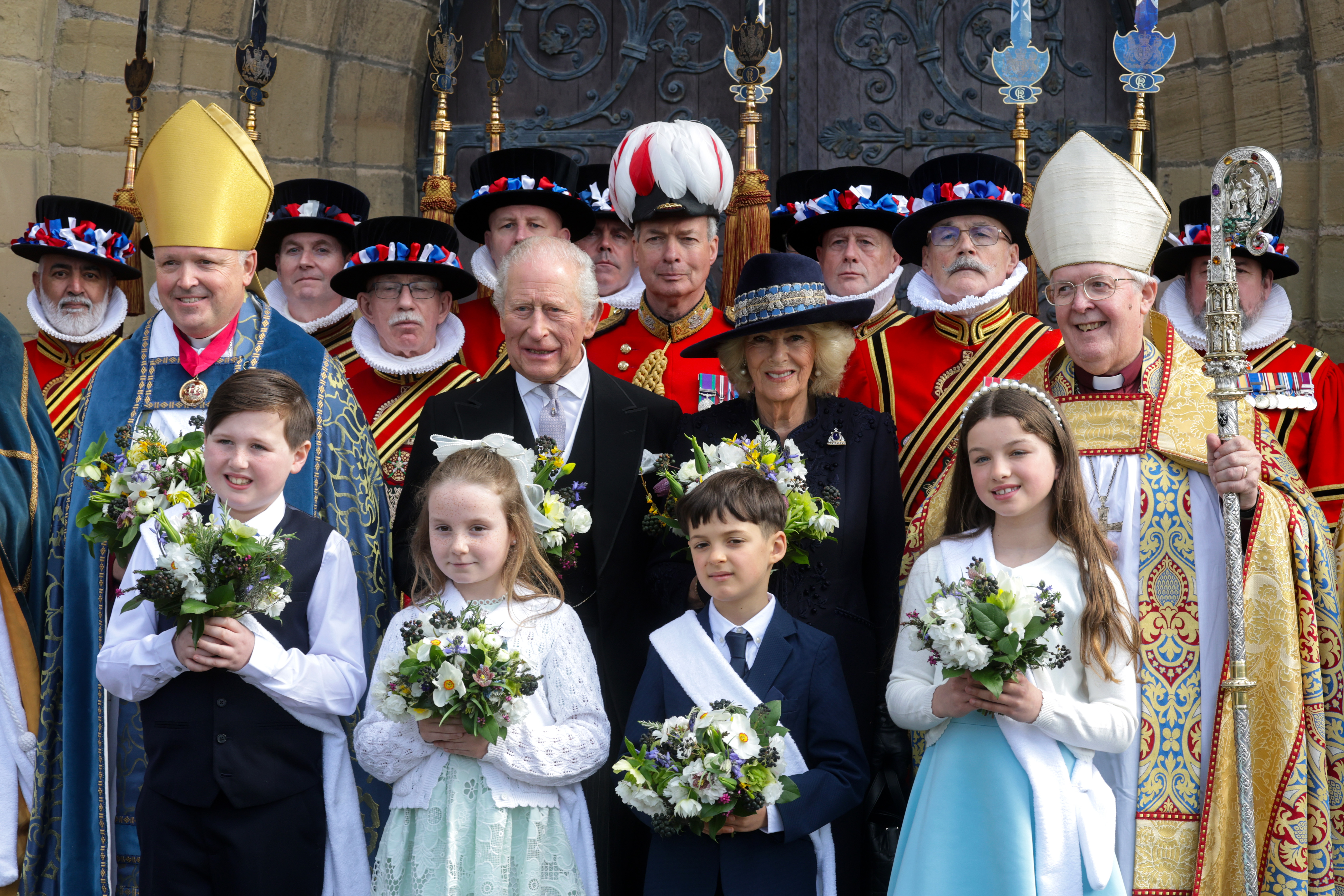 King Charles and Queen Camilla posing with beefeaters, clergymen and children outside a church