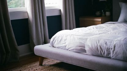 Best cooling mattresses hero image - the bottom corner of a white bed, long grey curtains in a darkened room 