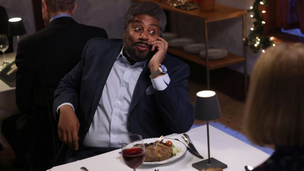 Kenan Thompson takes a phone call at dinner with an amused look on his face on Saturday Night Live, S50 E10.