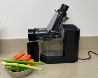 Philips Viva Masticating Juicer on counter with a bowl of vegetables including celery stalks, carrots and spinach leaves