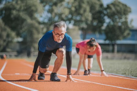 An older couple getting ready to sprint at a track and field stadium in the morning.