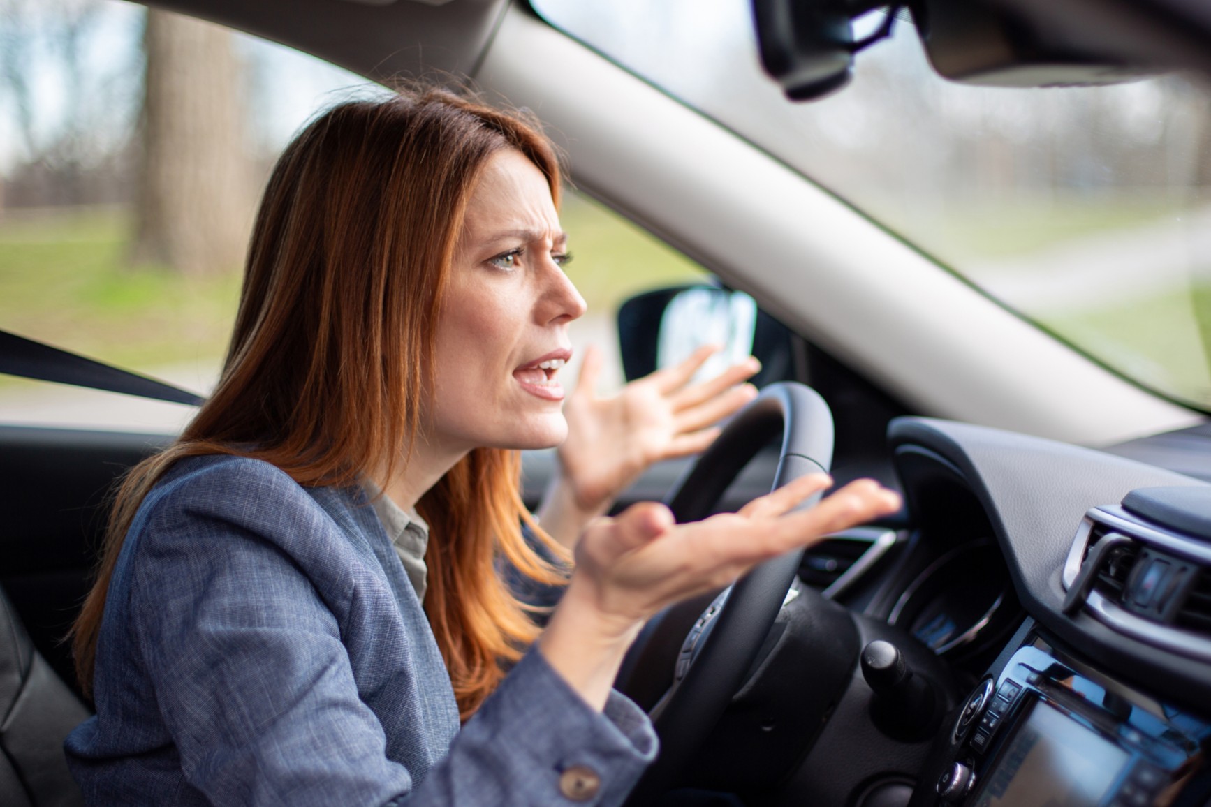 A woman gestures in frustration while driving a car.