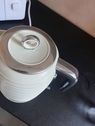 A cream kettle with stainless steel trims in front of a white microwave on a black counter