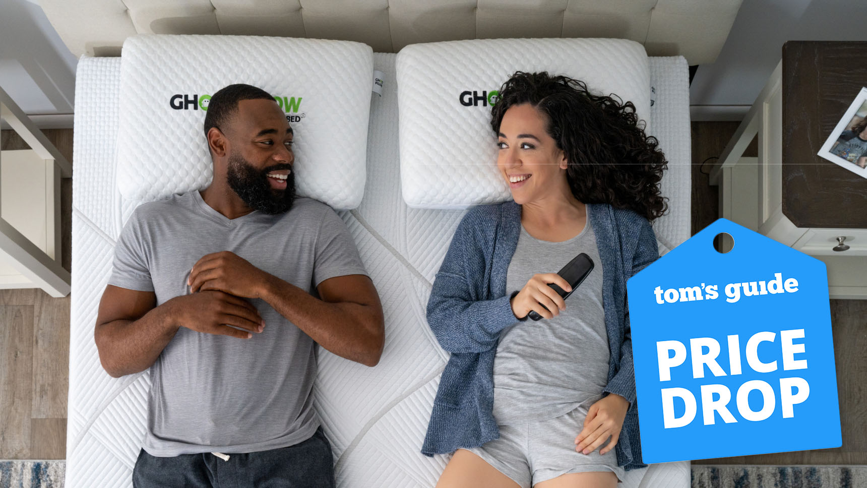 A bird's eye view of a man and woman lying on a GhostBed Massage Foam Mattress. In the bottom right, a Tom's Guide Price Drop deals graphic