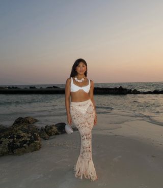 Woman on beach wears white bikini top and crochet skirt