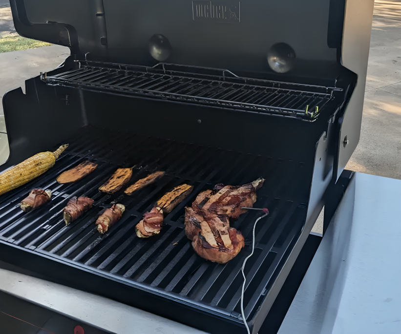 A Weber gas grill open with charred meat and vegetables on the griddle.