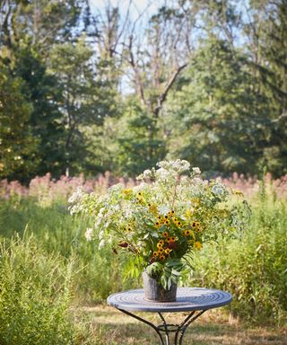 A container of white and yellow wild flowers on a table in a meadow