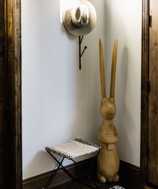 Entryway corner with decorative wall hook and hat, stylish rug, fabric chair and wood sculpted hare