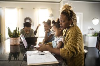 Mum working at home with child on her lap, and rest of the family sitting nearby