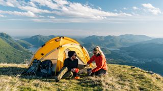 Couple camping on mountain top, prepare food and beverages next to tent