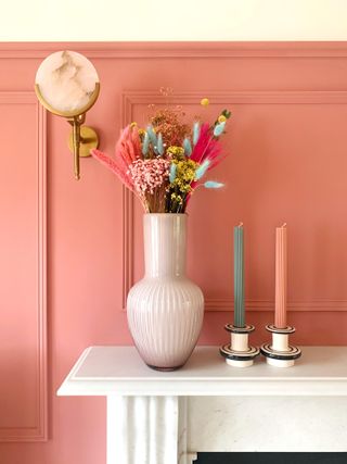 Decorated mantlepiece with dried flowers and candles against strawberry pink wall with trim