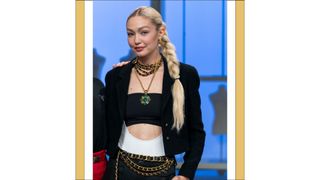 Host Gigi Hadid wears a black suit, crop top and gold chain belt in episode 207 of Next In Fashion.