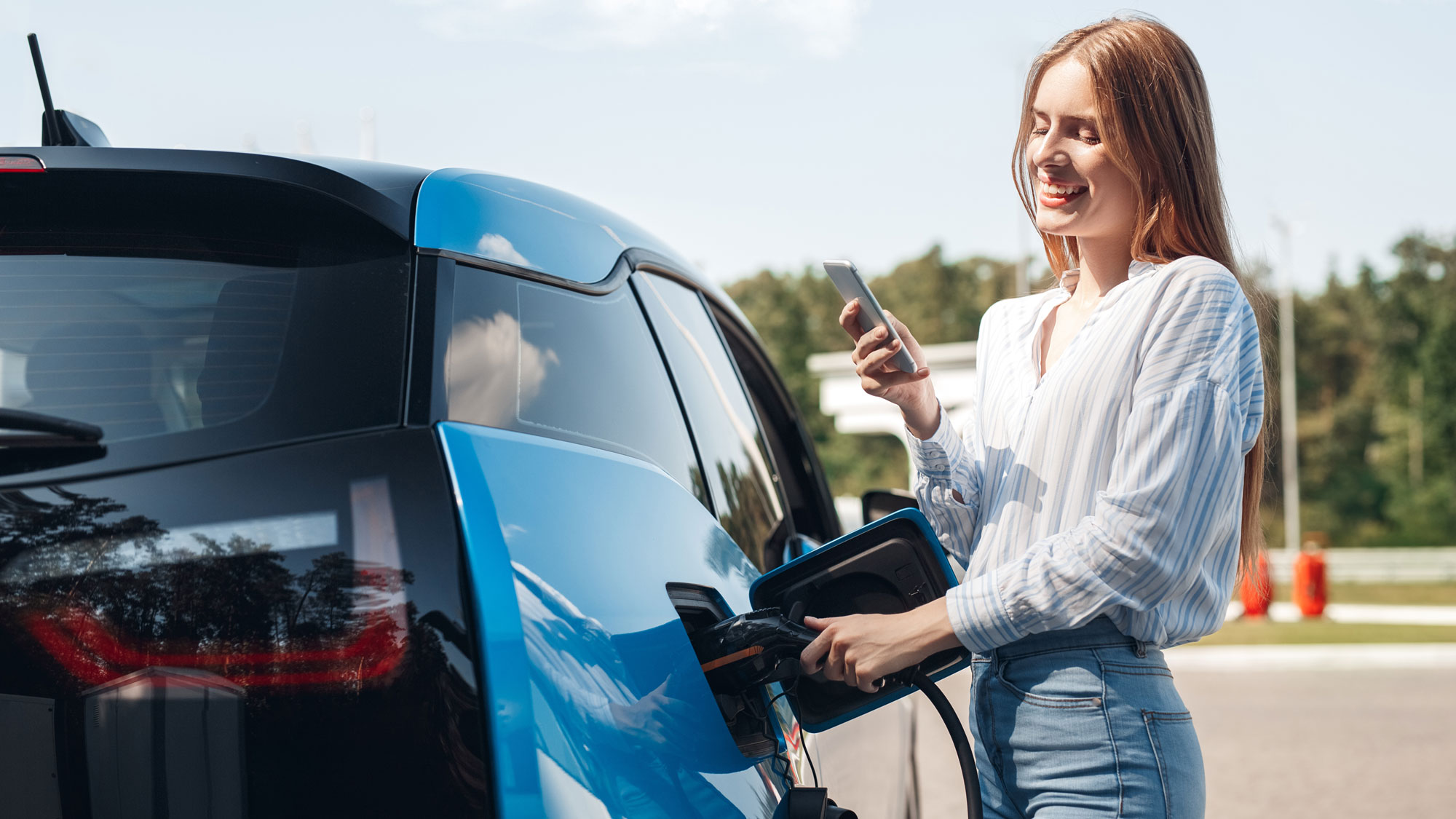 woman traveling by electric car having stop at charging station standing plugging cable