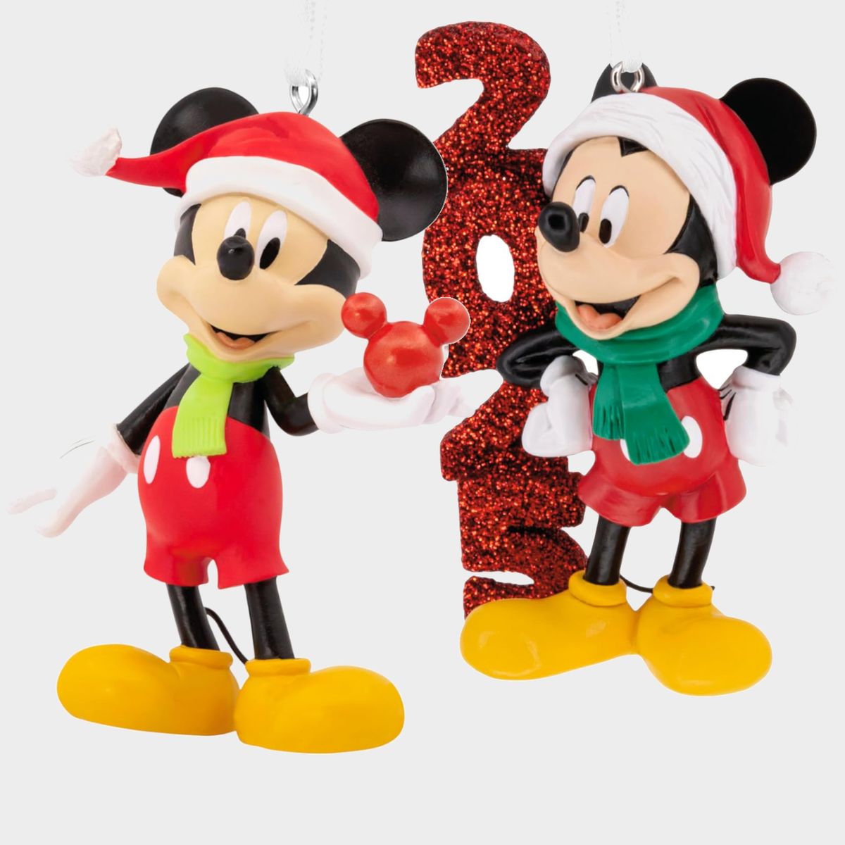 Ornaments of Mickey Mouse holding a Christmas bauble and leaning against a sparkly 2025, all on a plain background