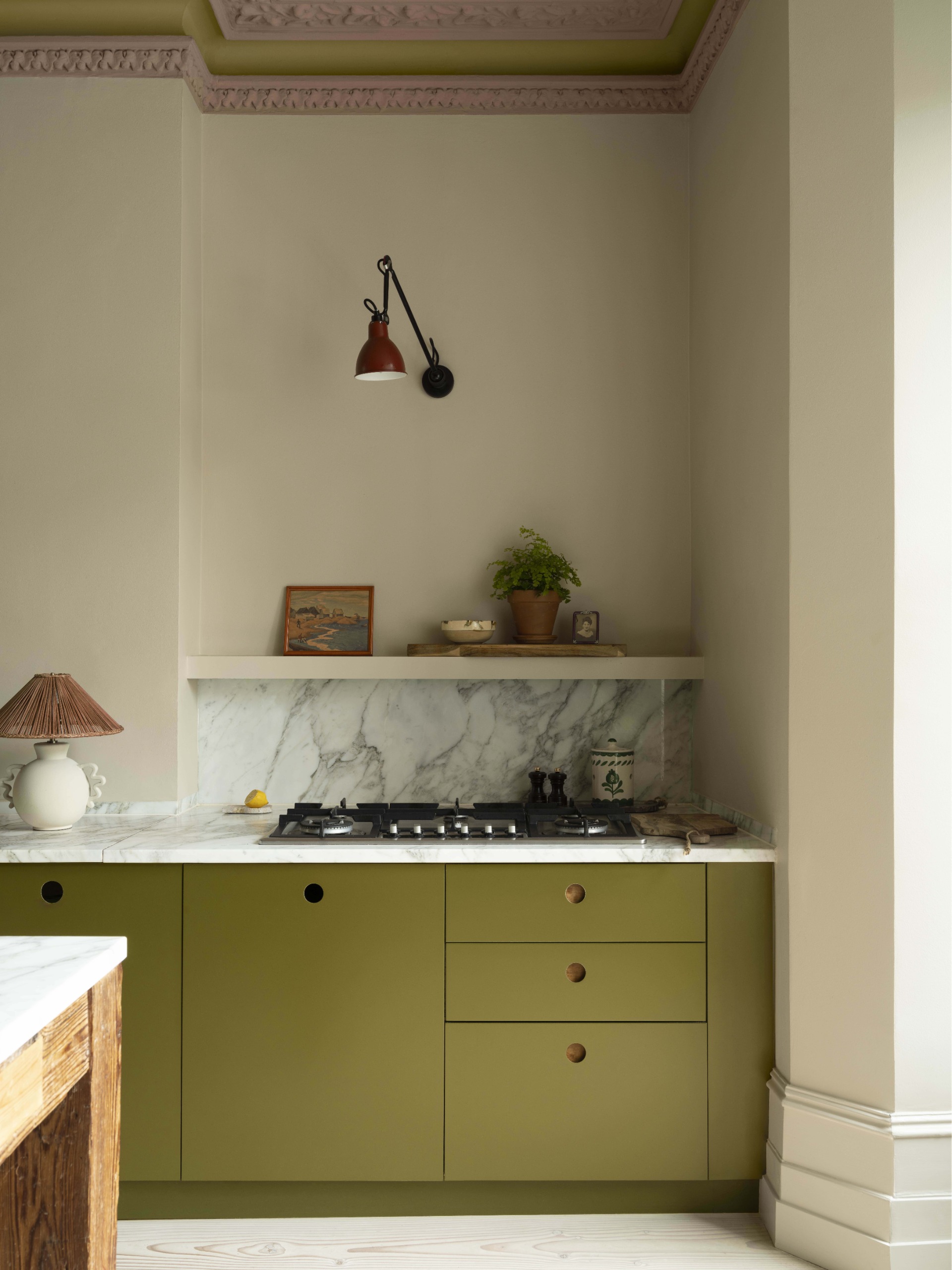 A modern kitchen with olive green counters, marble countertops and pale green walls