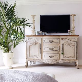 bedroom with white wall tv on wall and designed drawers