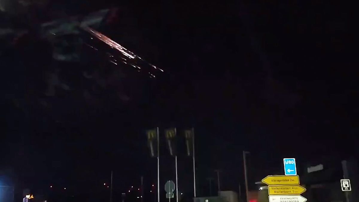 space junk burns up in a dark night sky over a city, leaving a large orange-yellow trail