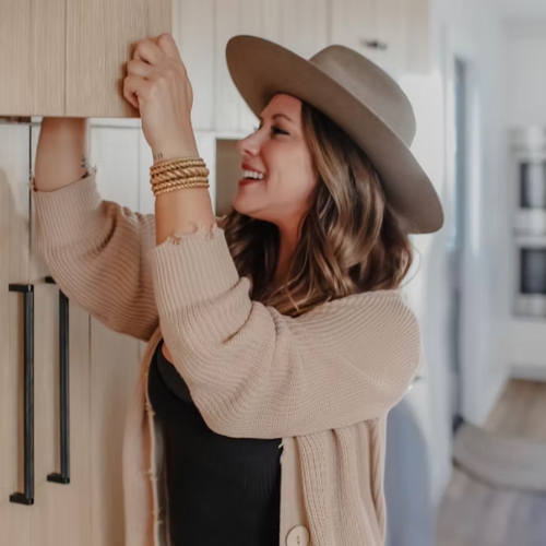 Image of a woman in a beige hat and sweater searching through an open cabinet.