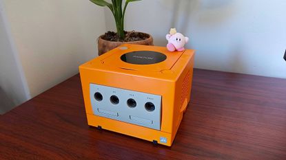 Spiced Orange Nintendo GameCube on woodgrain desk next to plant with Kirby figure sitting on top.