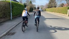 A child rider next to her mum riding on the road with the pavement to the side