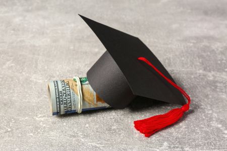  Graduation cap and banknotes on a light grey table