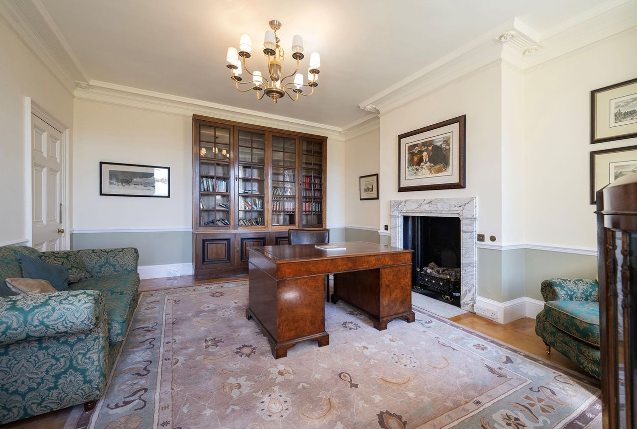The office has wooden desk and a large black fireplace next to it