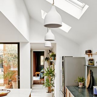 A white, modern open-plan kitchen with skylights and pendant light fixtures