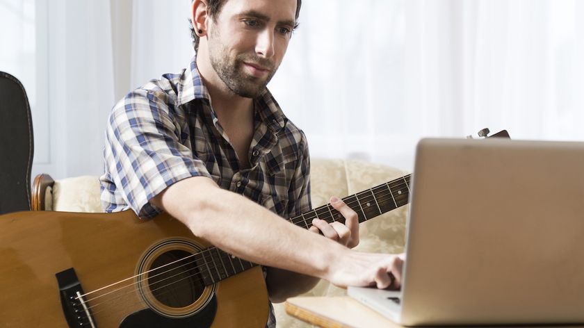 Man holding acoustic guitar in front of a silver laptop
