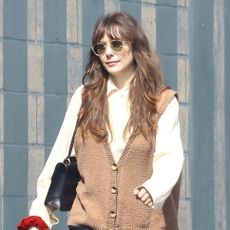 Elizabeth Olsen wearing a tan sweater vest, button-down shirt, jeans, and high-vamp pumps