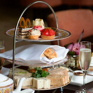 3-tiered tray containing sandwiches, savories and desserts on a table next to a glass of champagne