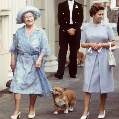 Queen Mother and Queen Elizabeth wearing blue dresses and white heels walking with a corgi behind them outside a building