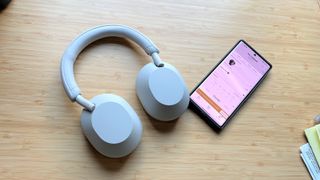 Listing image for the best headsets and headphones for working from home showing Sony WH-1000XM5 with iPhone on a wooden desktop