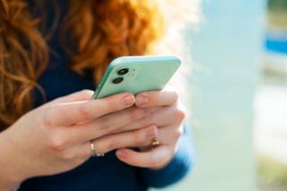 A woman with red hair holds onto a smart phone in a turquoise blue case