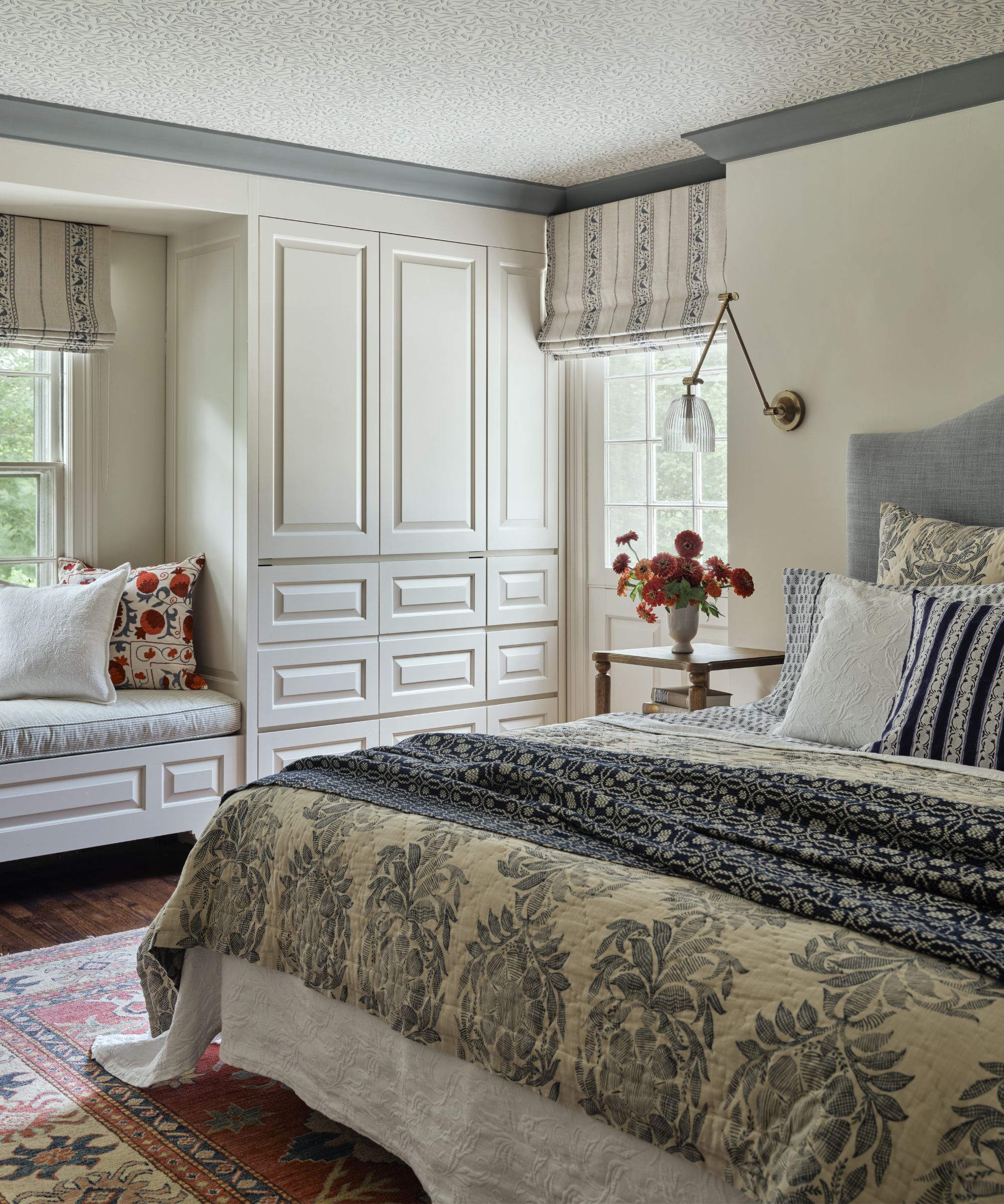 a light neutral and blue bedroom with wallpapered ceiling and patterned blue bed linens