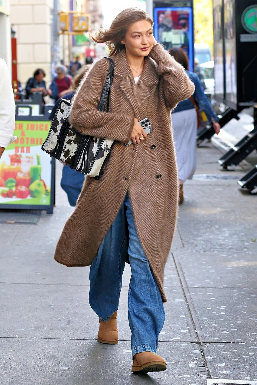 Gigi Hadid wearing a tan coat, baggy jeans, a cow-print bag, and Ugg boots