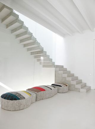 White room containing a white stairwell, with a striped coloured seating area at the bottom