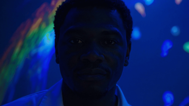 Firefly video created with prompt "the man looks at the camera chromatic prismatic reflections dance across his face"
