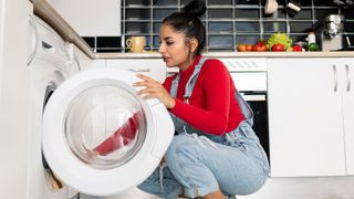 Woman crouched next to a washing machine in a kitchen